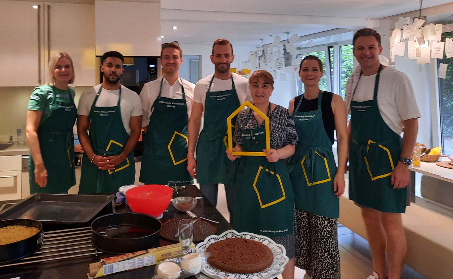 Group of people wearing aprons with baking equipment and cakes