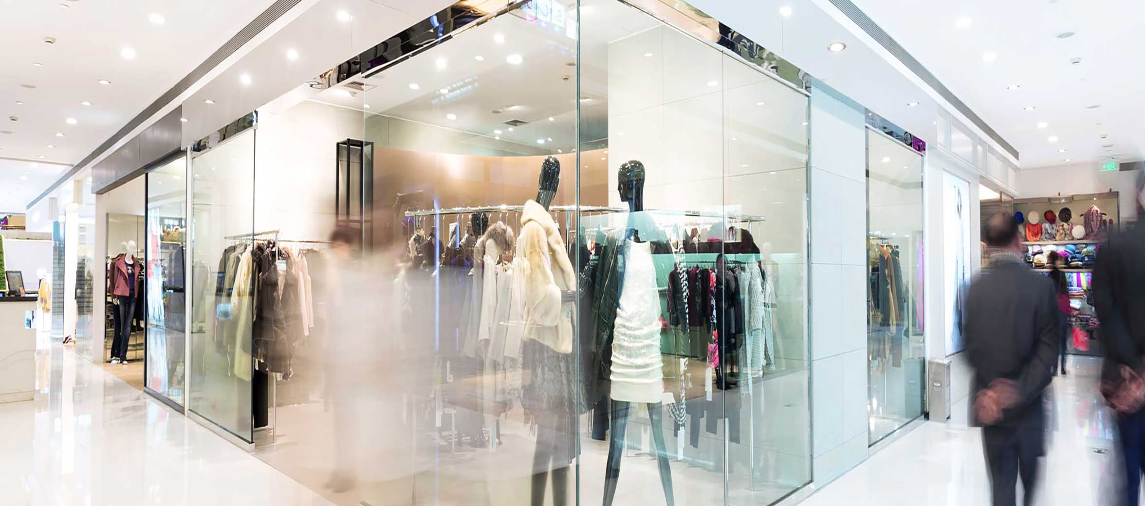 People walking past a clothing store with large glass windows in a shopping mall