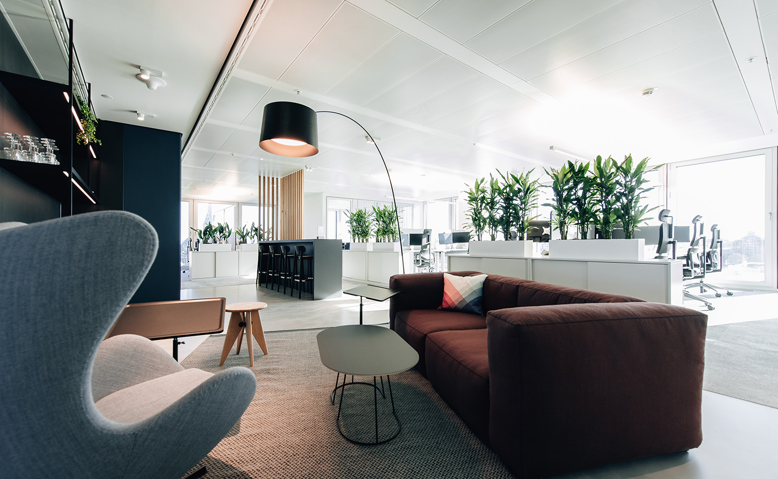Lounge mit grauem Sessel, dunkelrotem Sofa, Couchtischen und Lampe im Hamburger Büro