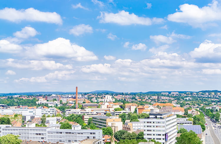 A vibrant city with a clear, sunny sky, featuring diverse tall buildings, streets lined with trees in residential areas