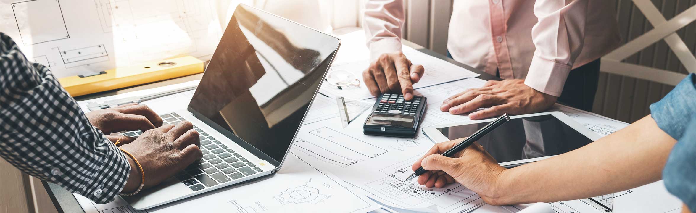 A team of diverse colleagues uses laptop and calculators to work on a project together