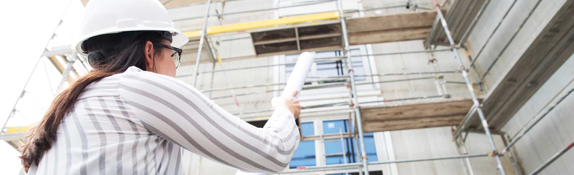 A construction manager with a white hard hat with a blue print in her hand on a construction site