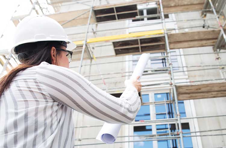 A construction manager with a white hard hat with a blue print in her hand on a construction site
