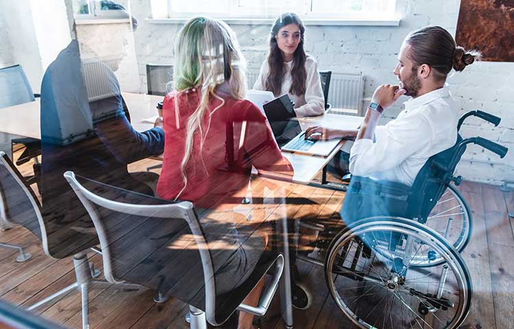 A group of diverse colleagues including a man in a wheel chair in the conference room