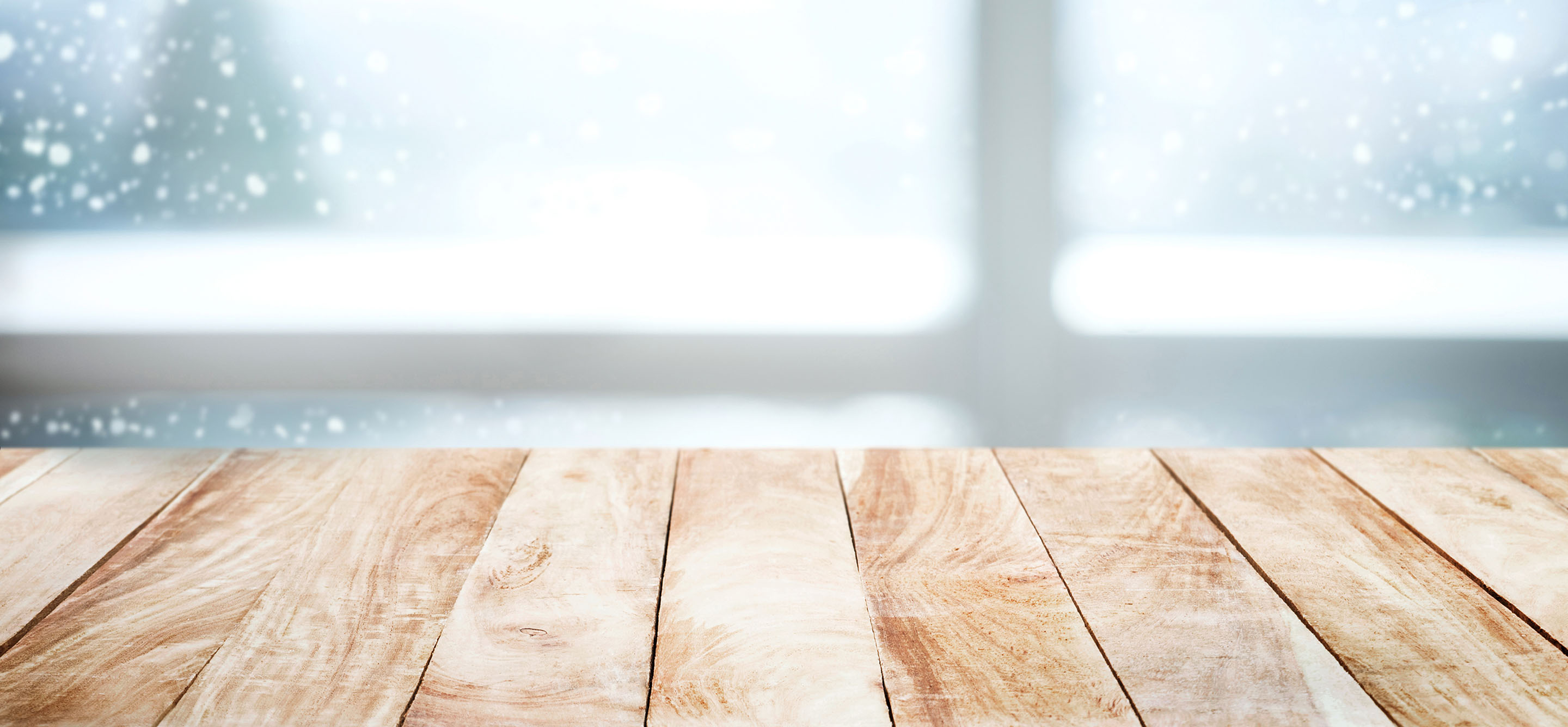 Empty wood table next to window view of pine tree in snow fall