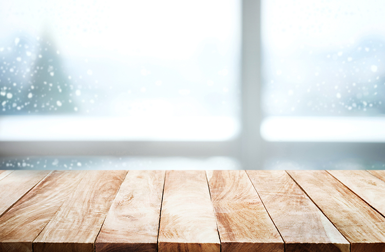 Leerer Holztisch neben dem Fenster mit Blick auf eine Kiefer im Schneefall