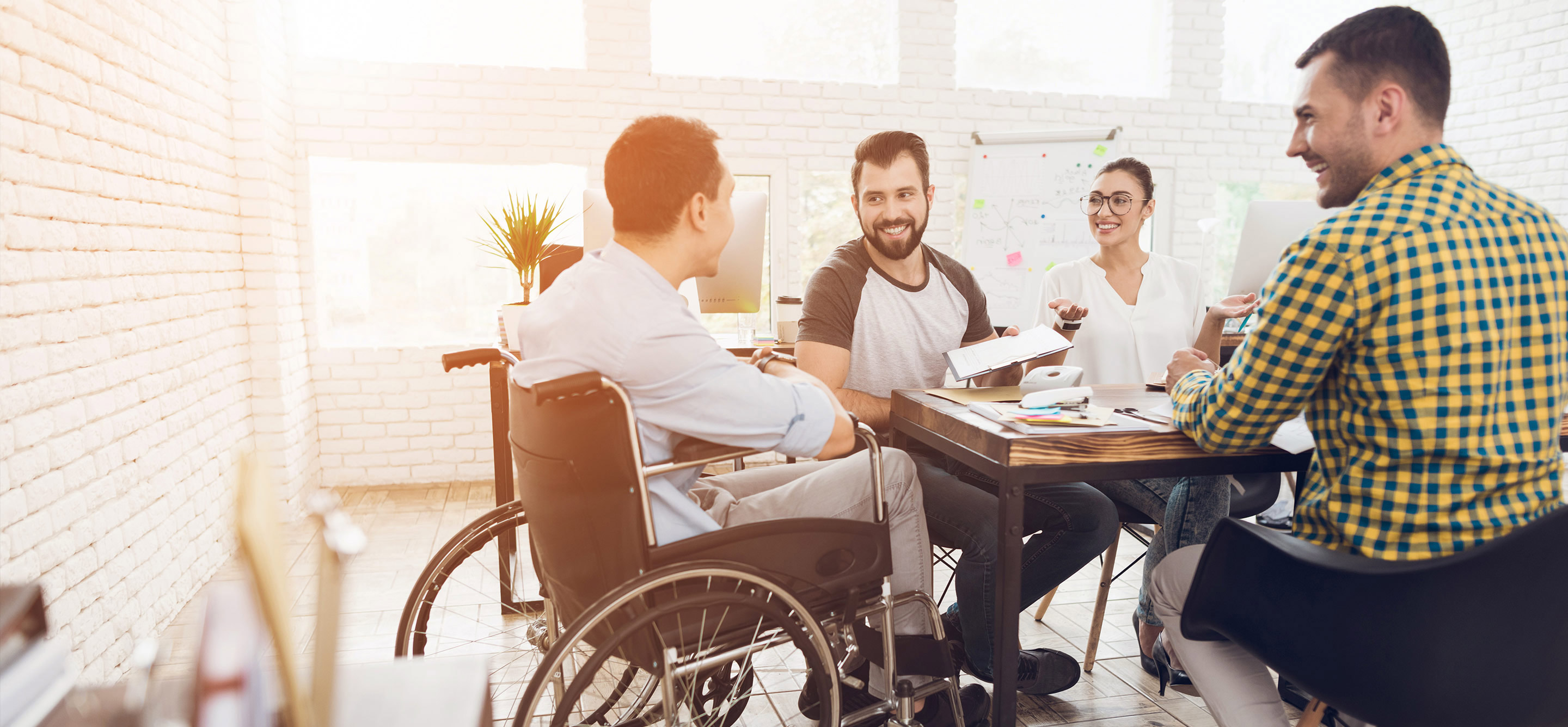 A man in a wheelchair communicates cheerfully with employees of the office during a business meeting