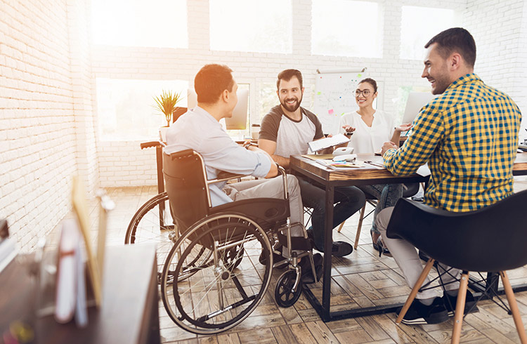 A man in a wheelchair communicates cheerfully with employees of the office during a business meeting