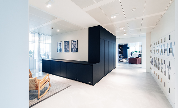Office with black cabinets, 3 portraits hanging on a white wall, and a large locker with the printed slogan Life is what we make it
