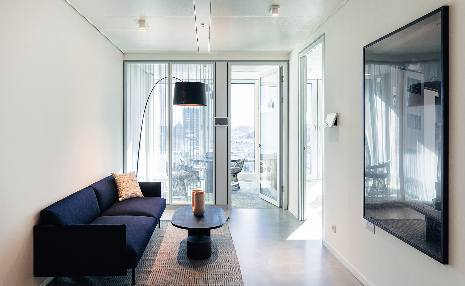 Lounge mit einem dunkelblauen Sofa, einem Couchtisch, einer Stehlampe und einem Wandposter